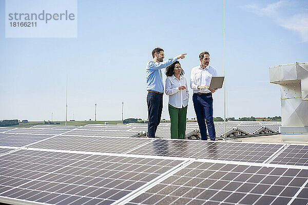 Geschäftsmann deutet auf Kollegen  die über Solarpaneele auf dem Dach diskutieren