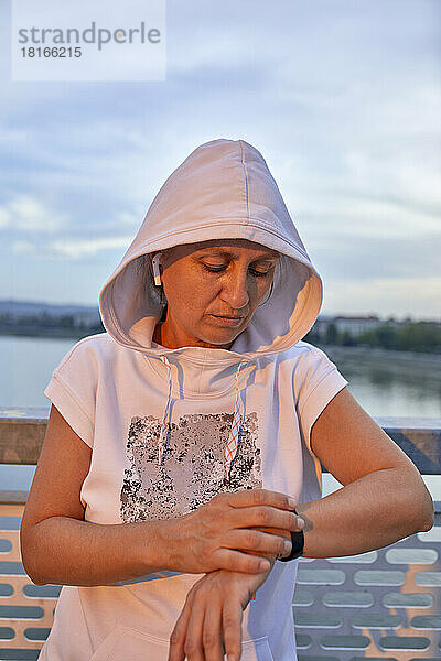 Frau trägt Kapuzenshirt und prüft den Puls auf der Smartwatch