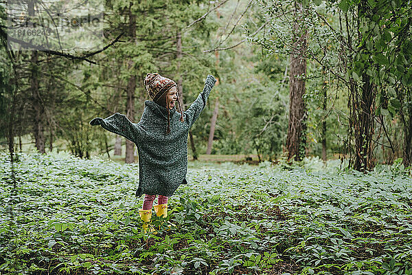 Glückliches Mädchen in übergroßem Pullover  das inmitten des Waldes steht