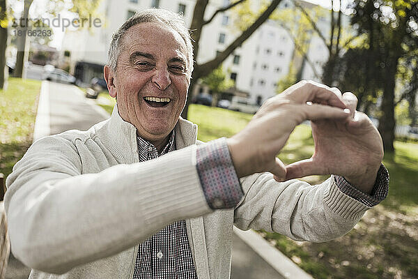 Glücklicher älterer Mann  der mit der Hand auf dem Fußweg eine Herzform macht