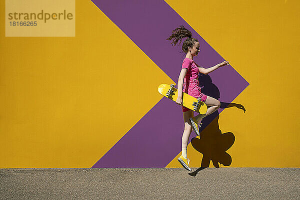 Frau mit Skateboard springt vor gemusterte Wand