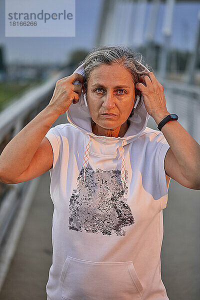 Selbstbewusste Frau mit kabellosen In-Ear-Kopfhörern und Kapuzenshirt