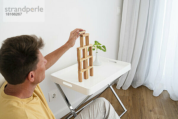 Mature man building wooden block tower on coffee table at home
