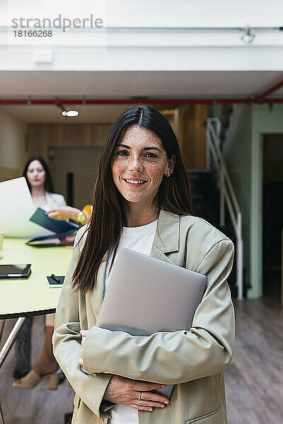 Porträt einer lächelnden brünetten Geschäftsfrau mit Laptop im Büro
