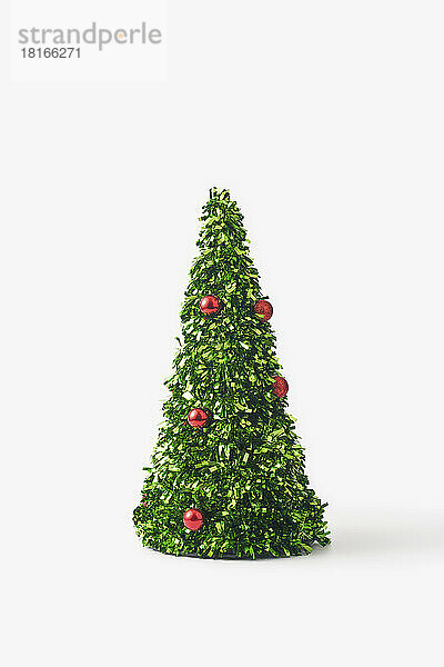 Kleiner Weihnachtsbaum aus grünem Konfetti und roten Kugeln vor weißem Hintergrund