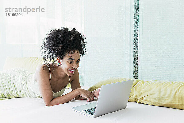 Happy woman lying on bed and using laptop at home