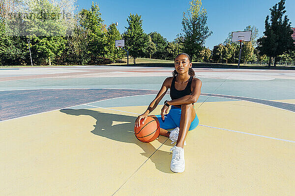 Selbstbewusste Sportlerin mit Basketball sitzt auf dem Platz