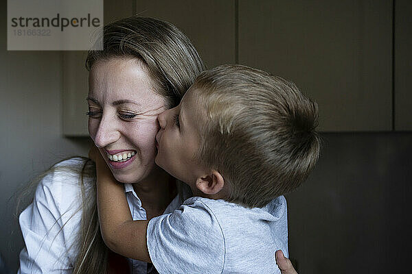 Boy kissing happy mother in kitchen