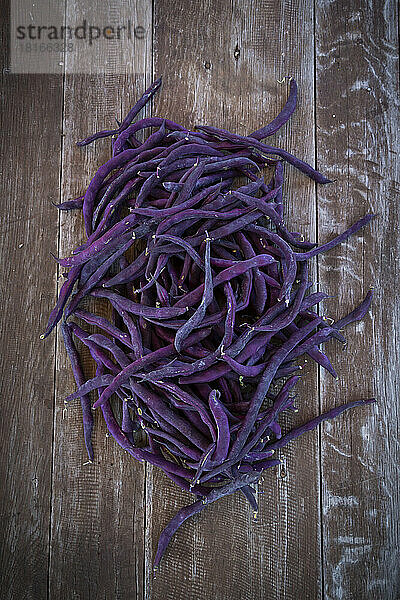 Frisch geerntete violette Bohnen (Phaseolus vulgaris) liegen auf einer Holzoberfläche