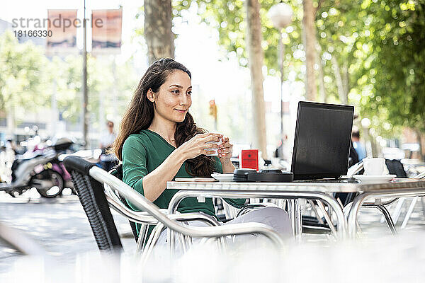 Lächelnde Frau benutzt Laptop im Straßencafé