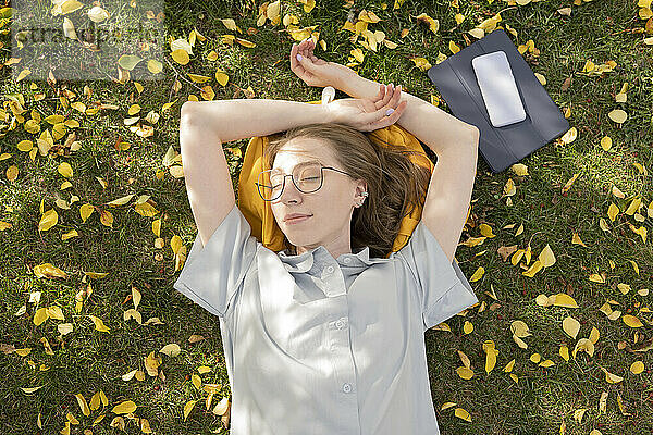 Junge Frau liegt mit geschlossenen Augen im Herbstpark