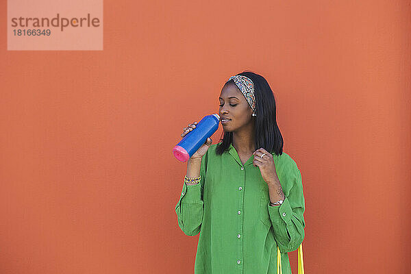 Junge Frau trinkt Wasser vor orangefarbener Wand