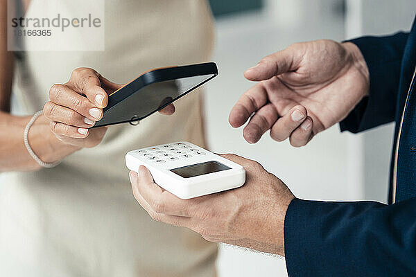 Hand eines Verkäufers mit Kreditkartenleser und zahlender Frau