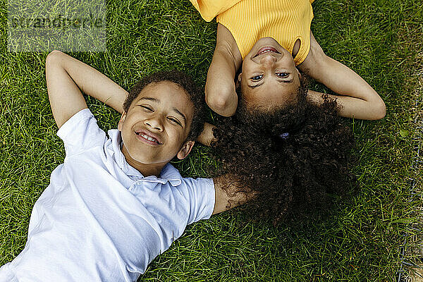 Smiling boy and girl with hands behind head lying on grass