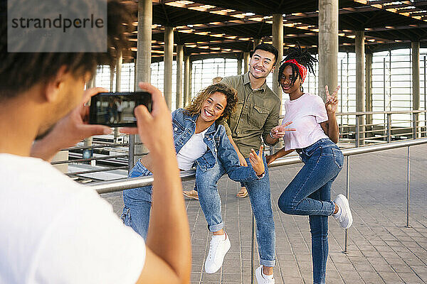 Young man photographing friends through smart phone at railroad station