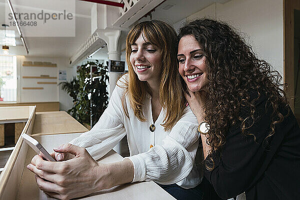 Zwei glückliche Geschäftsfrauen teilen sich ihr Mobiltelefon im Büro
