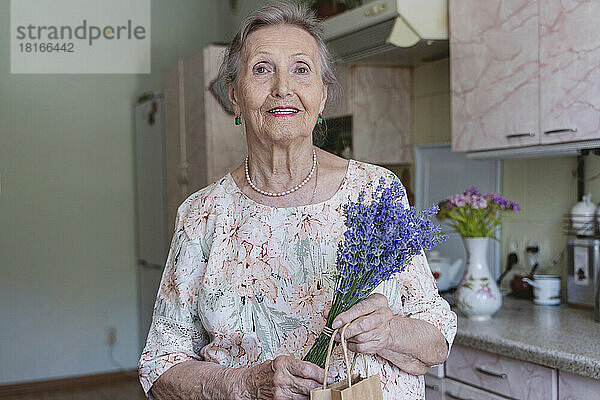 Lächelnde ältere Frau mit einem Strauß Lavendelblüten zu Hause