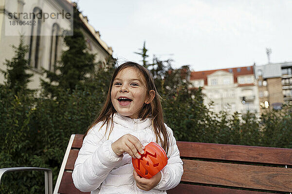 Glückliches Mädchen mit Kürbiskorb sitzt auf Bank im Park