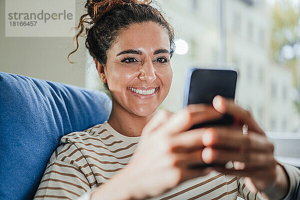 Lächelnde Frau  die zu Hause Textnachrichten auf dem Mobiltelefon sendet