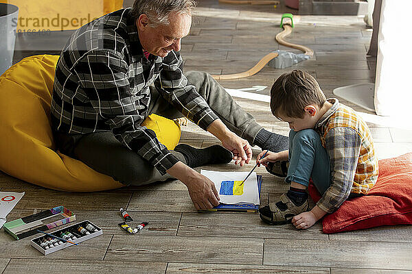 Glücklicher Großvater bringt seinem Enkel zu Hause das Zeichnen der ukrainischen Flagge bei