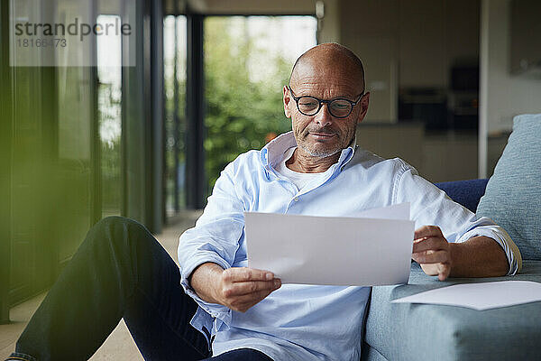 Älterer Mann liest Dokumente  sitzt zu Hause auf dem Sofa