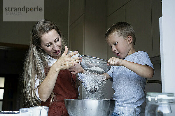 Mutter und Sohn sieben Mehl für die Kuchenzubereitung zu Hause