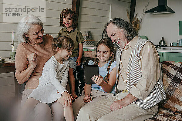 Glückliche Großeltern mit Kindern  die zu Hause einen Tablet-PC schauen