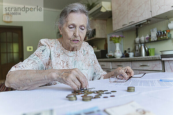 Ältere Frau zählt Ersparnisse und erledigt zu Hause Papierkram