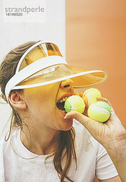 Sportswoman in sun visor biting tennis ball