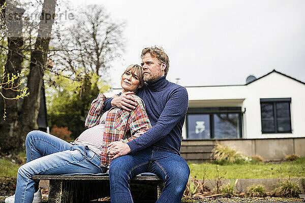 Reifer Mann sitzt mit schwangerer Frau vor dem Haus auf dem Steg