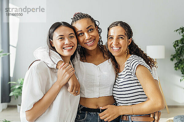 Happy multiracial roommates with arms around in living room