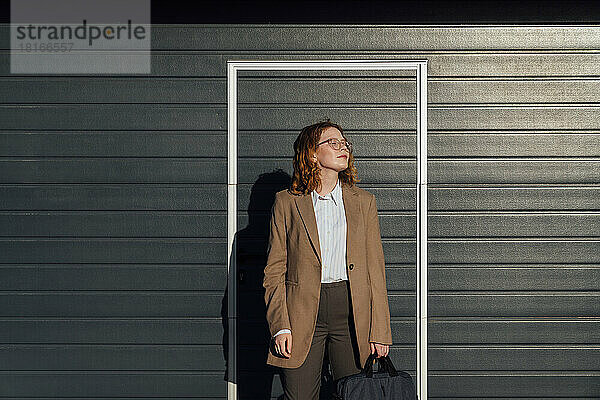 Junge Geschäftsfrau mit geschlossenen Augen vor einer schwarzen Wellwand an einem sonnigen Tag