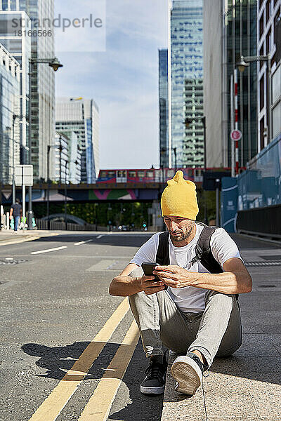 Mann benutzt Smartphone und sitzt auf Fußweg in der Stadt