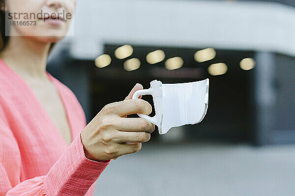 Hand einer Frau  die eine zerbrochene Kaffeetasse hält