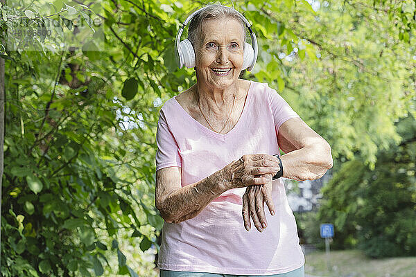 Glückliche ältere Frau mit Smartwatch  die im Park Musik über Kopfhörer hört