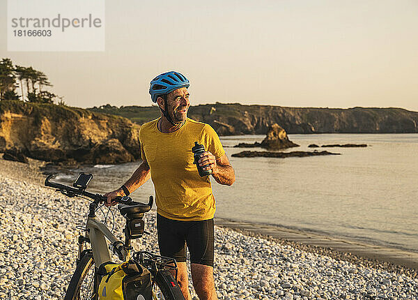 Glücklicher Mann mit Fahrrad und Wasserflasche am Strand