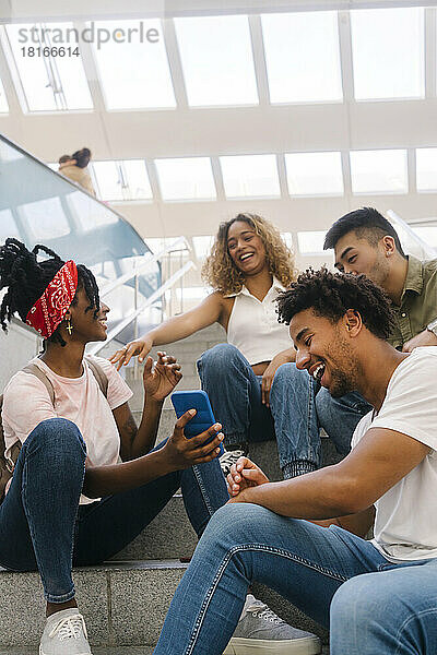 Gemischtrassige Freunde schauen auf ihr Smartphone und lachen auf der Treppe