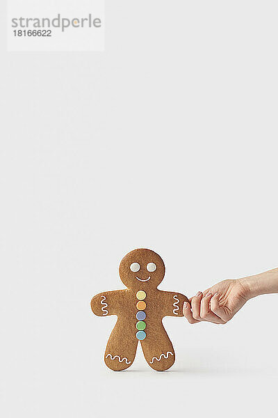 Hand of woman holding freshly backed gingerbread cookie against white background