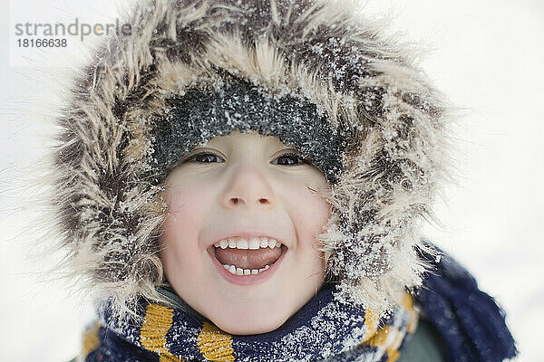 Netter Junge mit Fellkapuze  der im Winter lacht