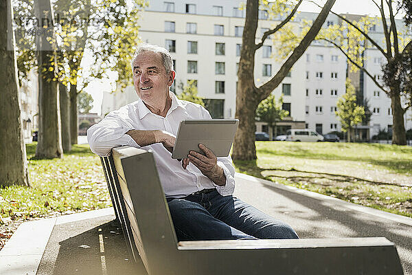 Nachdenklicher älterer Mann mit Tablet-PC sitzt auf Bank