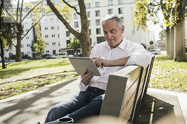 Älterer Mann sitzt mit Tablet-PC auf Bank