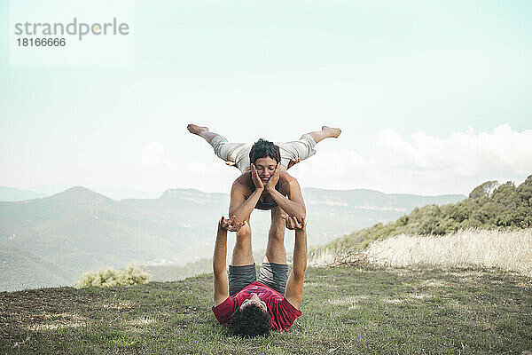 Couple doing acroyoga on mountain in front of sky