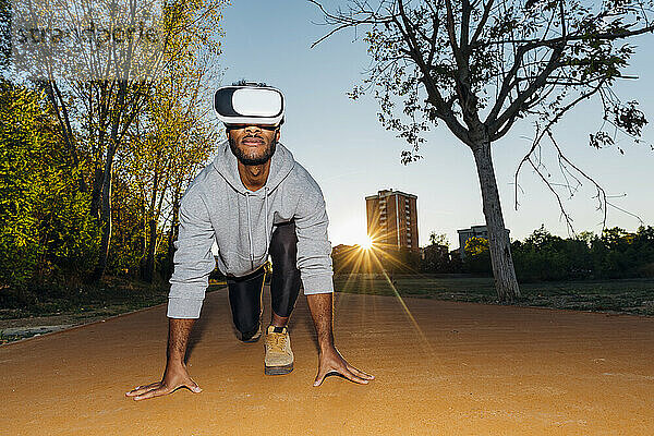 Sportler mit VR-Brille kniet an der Startlinie im Park