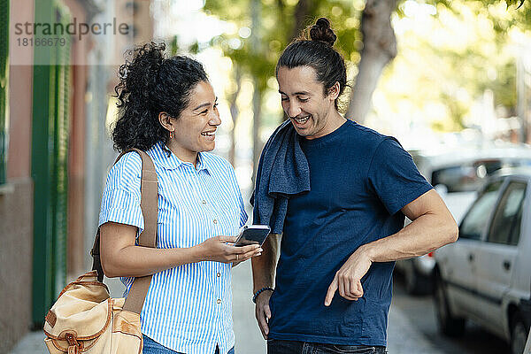 Lächelnde Frau teilt Smartphone mit Freund auf Fußweg