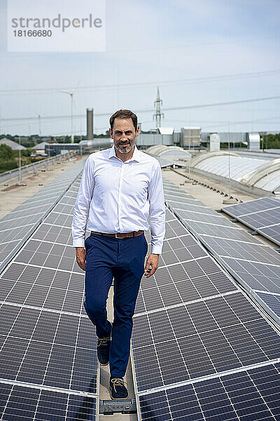 Reifer Geschäftsmann spaziert zwischen Sonnenkollektoren auf dem Dach