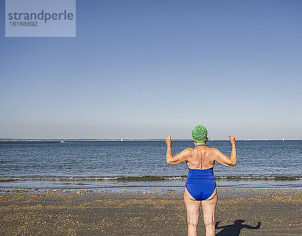 Ältere Frau im Badeanzug blickt an einem sonnigen Tag auf das Meer