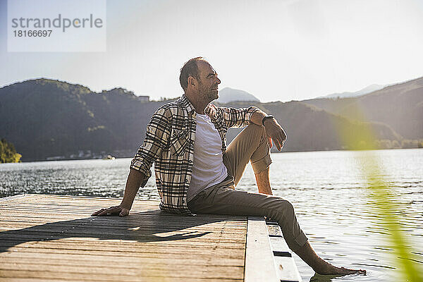 Nachdenklicher Mann sitzt auf der Anlegestelle über dem See