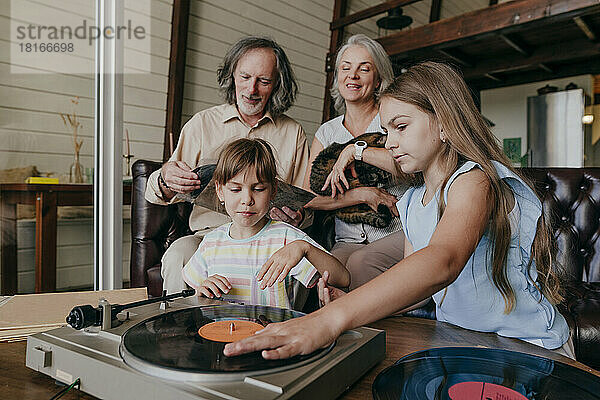 Enkelinnen spielen mit den Großeltern zu Hause Musik auf einem Vinyl-Plattenspieler