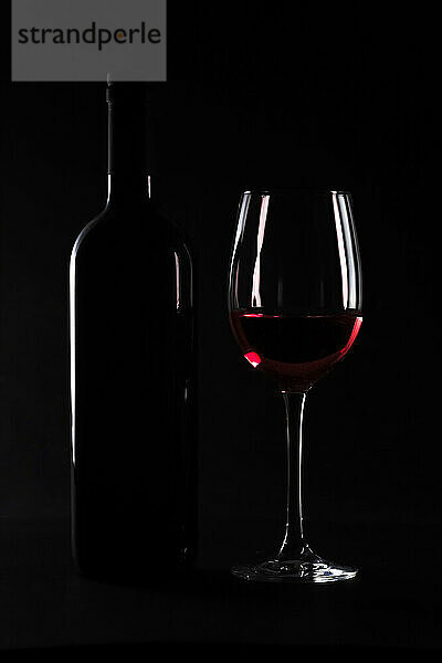 Dunkle Studioaufnahme einer Flasche und eines Glases Rotwein