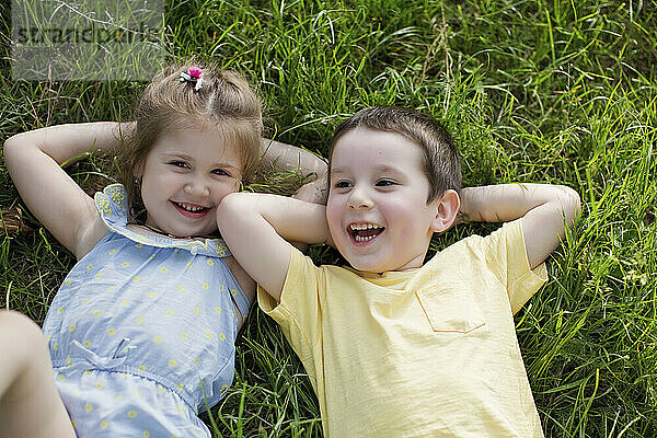 Glücklicher Junge und Schwester entspannen sich im Gras im Park
